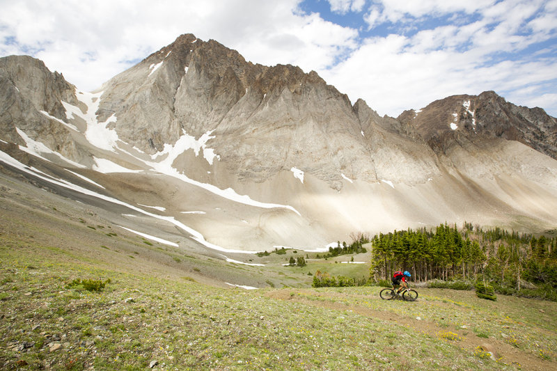 Rider on a singletrack trail below a snow-streaked mountain range near Sun Valley, ID